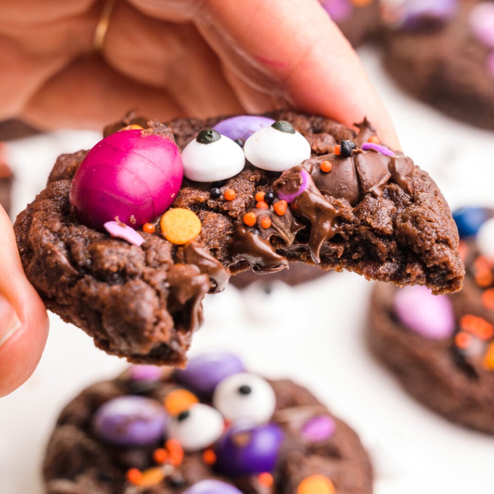 A hand holds a Halloween cookie with a bite taken out, revealing lots of chocolate chips inside.