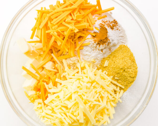 Ingredients like vegan cheese, nutritional yeast flakes, and seasonings are in a bowl.