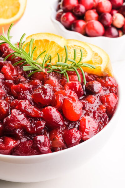 A bowl of vegan cranberry sauce sits in front of an orange and a bowl of fresh cranberries.