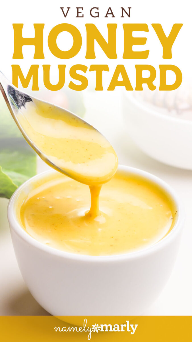 Creamy vegan honey mustard sauce in a white bowl with a spoon drizzling the sauce.