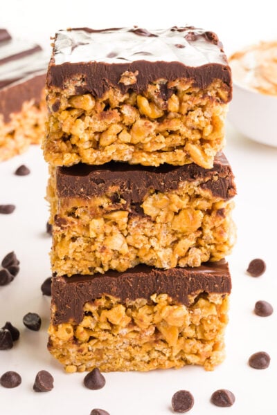 A stack of vegan schotcharoos has chocolate chips around it. There are more treats in the background.