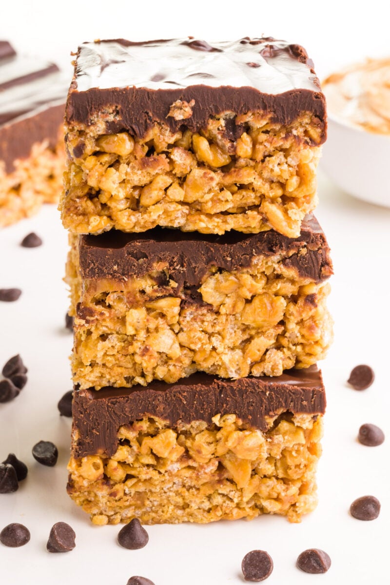 A stack of vegan schotcharoos has chocolate chips around it. There are more treats in the background.