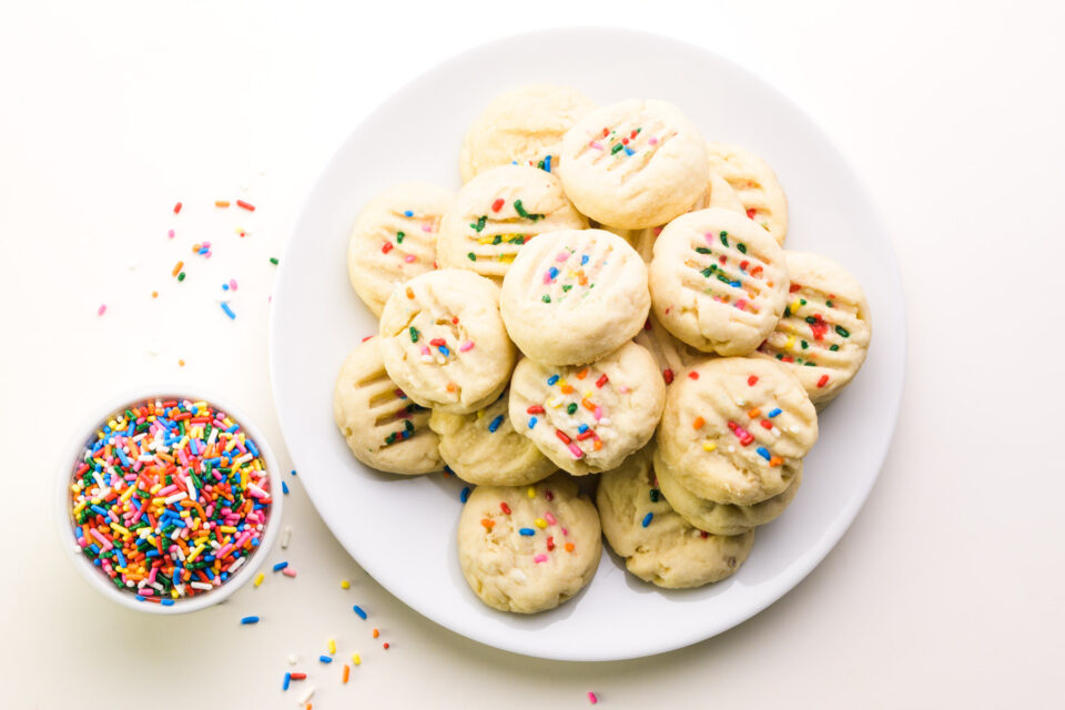Looking down on a plate of shortbread cookies. There is a bowl of sprinkles next to it.
