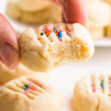 A hand holds a shortbread cookie with a bite taken out.