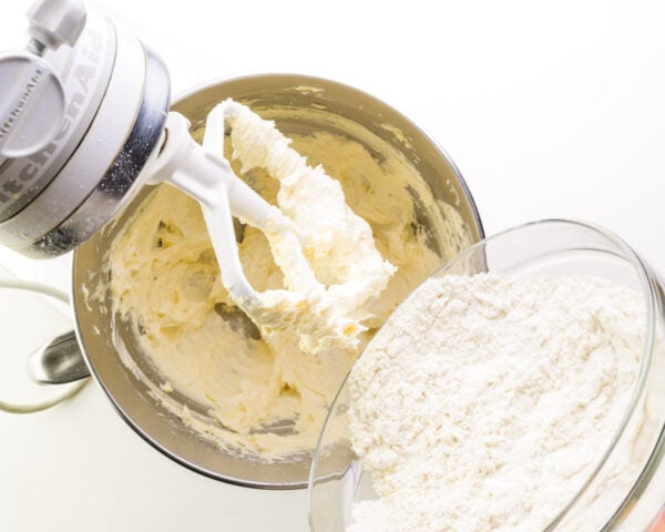 Flour is being added to a stand mixer bowl with whipped butter.