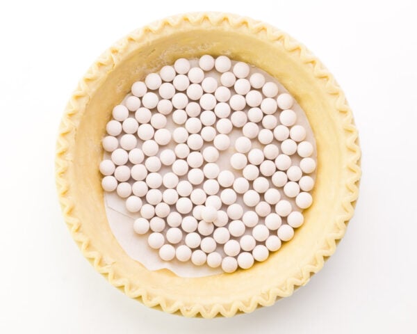 Pie weights are on a sheet of parchment paper in the bottom of a pie crust.