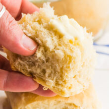 A hand holds a vegan dinner rolls with a bit of butter on top.