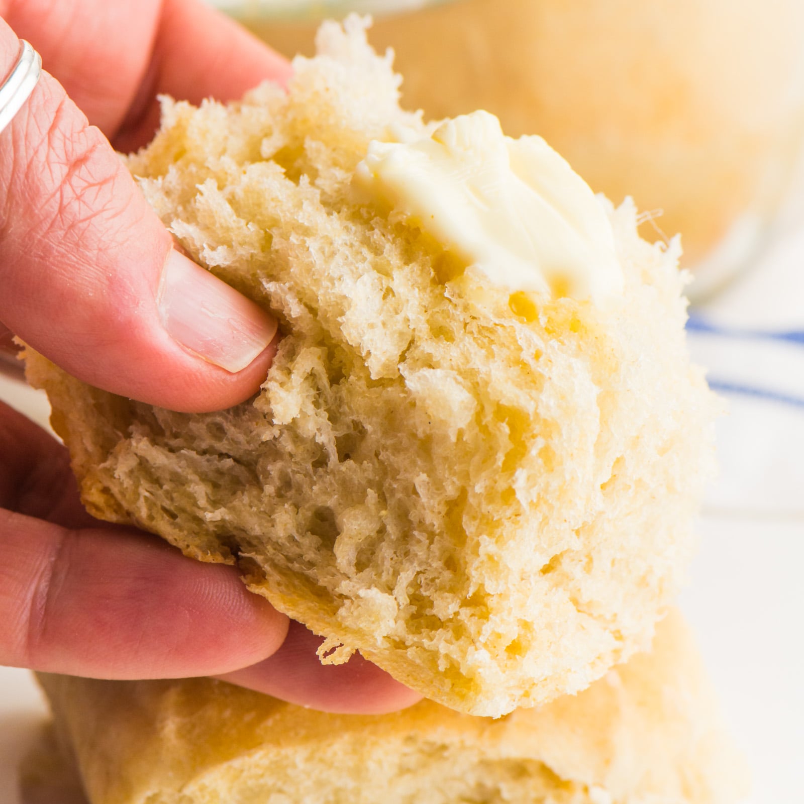 A hand holds a vegan dinner rolls with a bit of butter on top.