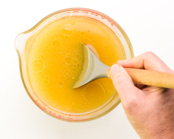 A hand holds a spatula, stirring a mixture of water, applesauce, and other ingredients.