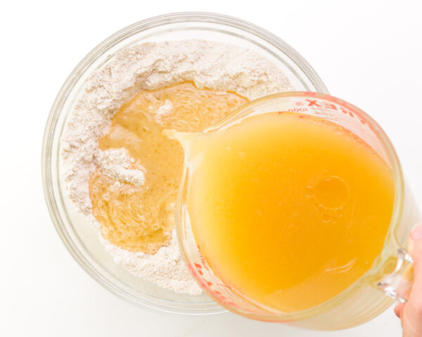 Wet ingredients are being poured into a bowl with dry ingredients to make cake batter.