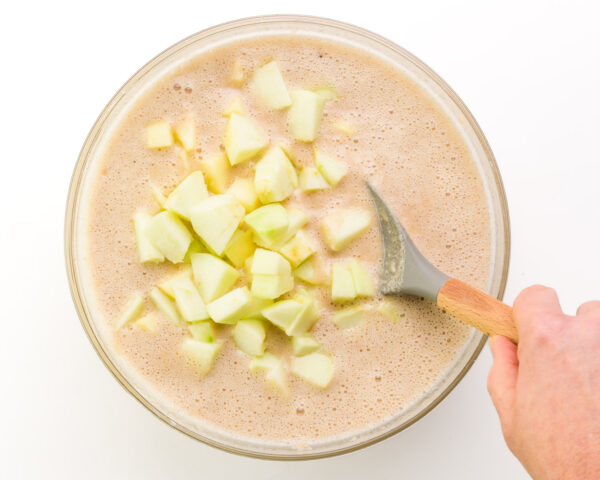 Chopped apples are being stirred into a cake batter.