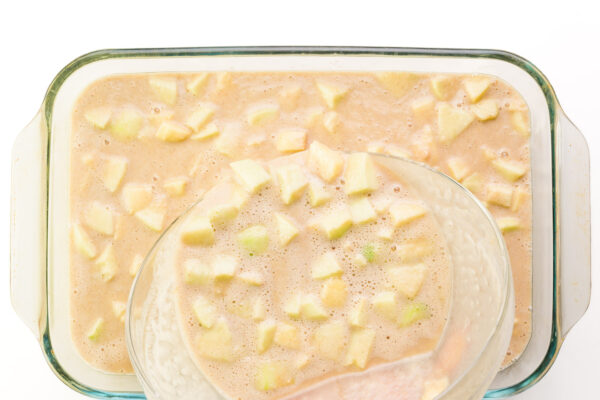 Cake batter with apple bits is being poured into a 9x13 cake pan.