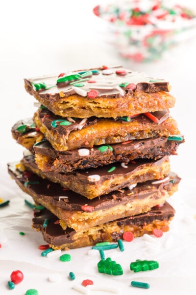 A stack of vegan Christmas crack pieces sits around sprinkles and a bowl of sprinkles in the background.