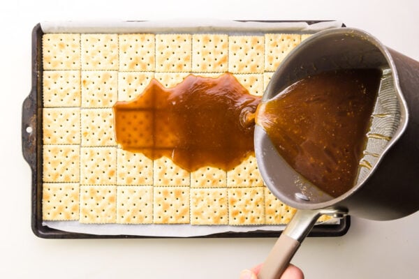 A caramel mixture is being poured over crackers in a pan.