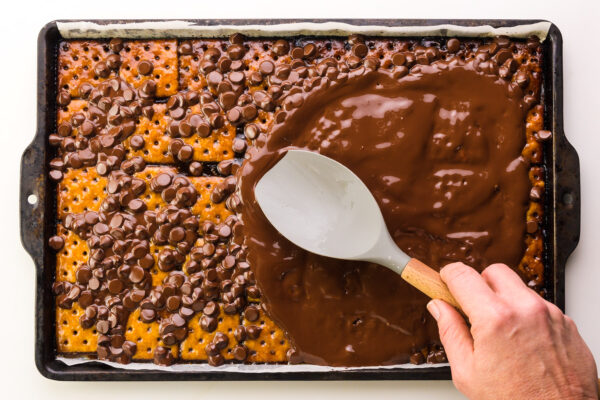 A hand holds a spatula, spreading melted chocolate chips in a pan.