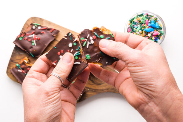 Two hands holds Christmas crack, breaking it into pieces.