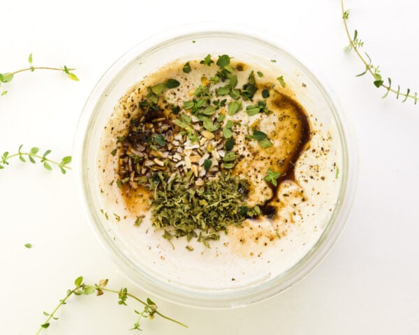 Seasonings and sauce has been added to sour cream in a bowl. Fresh herbs surround the bowl.