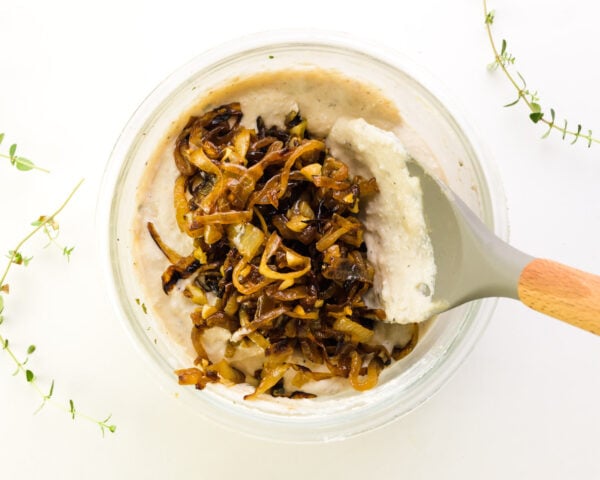A spatula is stirring caramelized onions into a creamy sauce.