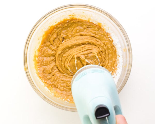 An electric mixer is beating a peanut butter mixture in a bowl.