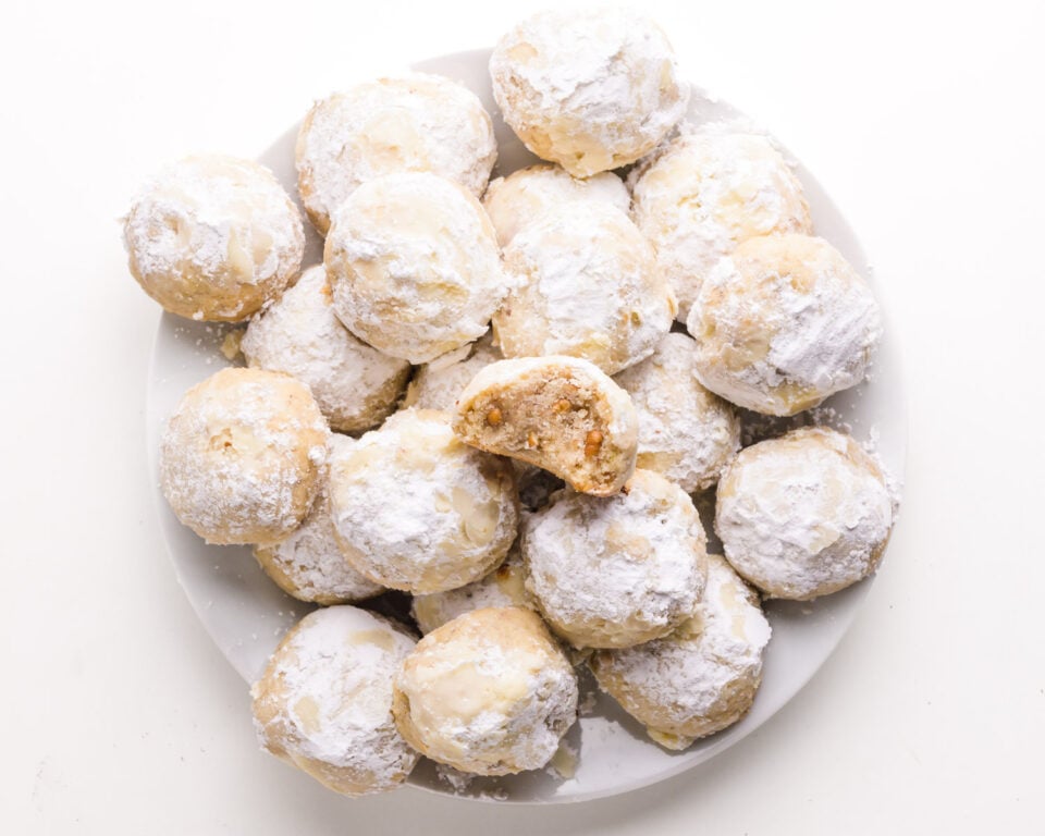 A plate of vegan cookies, one with a bite taken out, sits on a white counter.