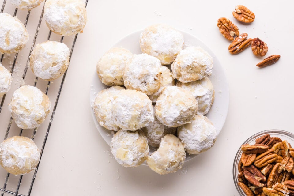 Looking down on vegan wedding cookies on a plate. There are pecans and a wire rack with more cookies nearby.