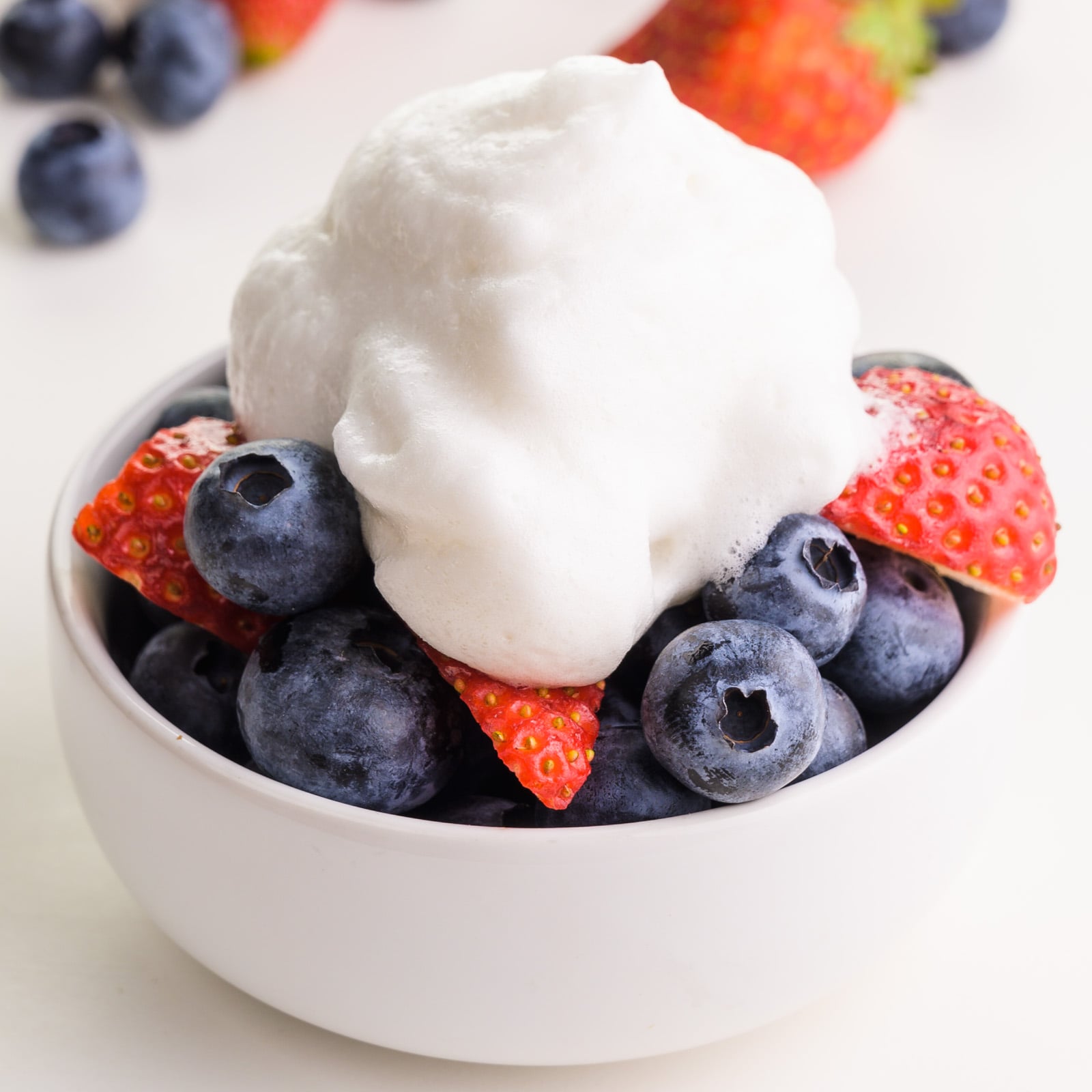 Whipped cream sits on top of a bowl of fresh fruit.