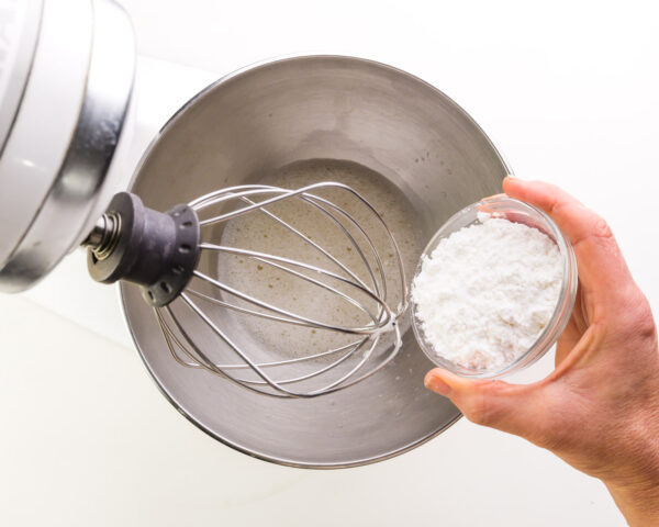 Cream of tartar is being added to a mixing bowl with a liquid ingredient.