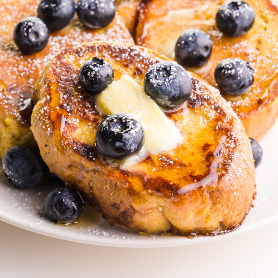 A closeup of a slice of Just Egg French Toast with blueberries, melted vegan butter, and maple syrup.