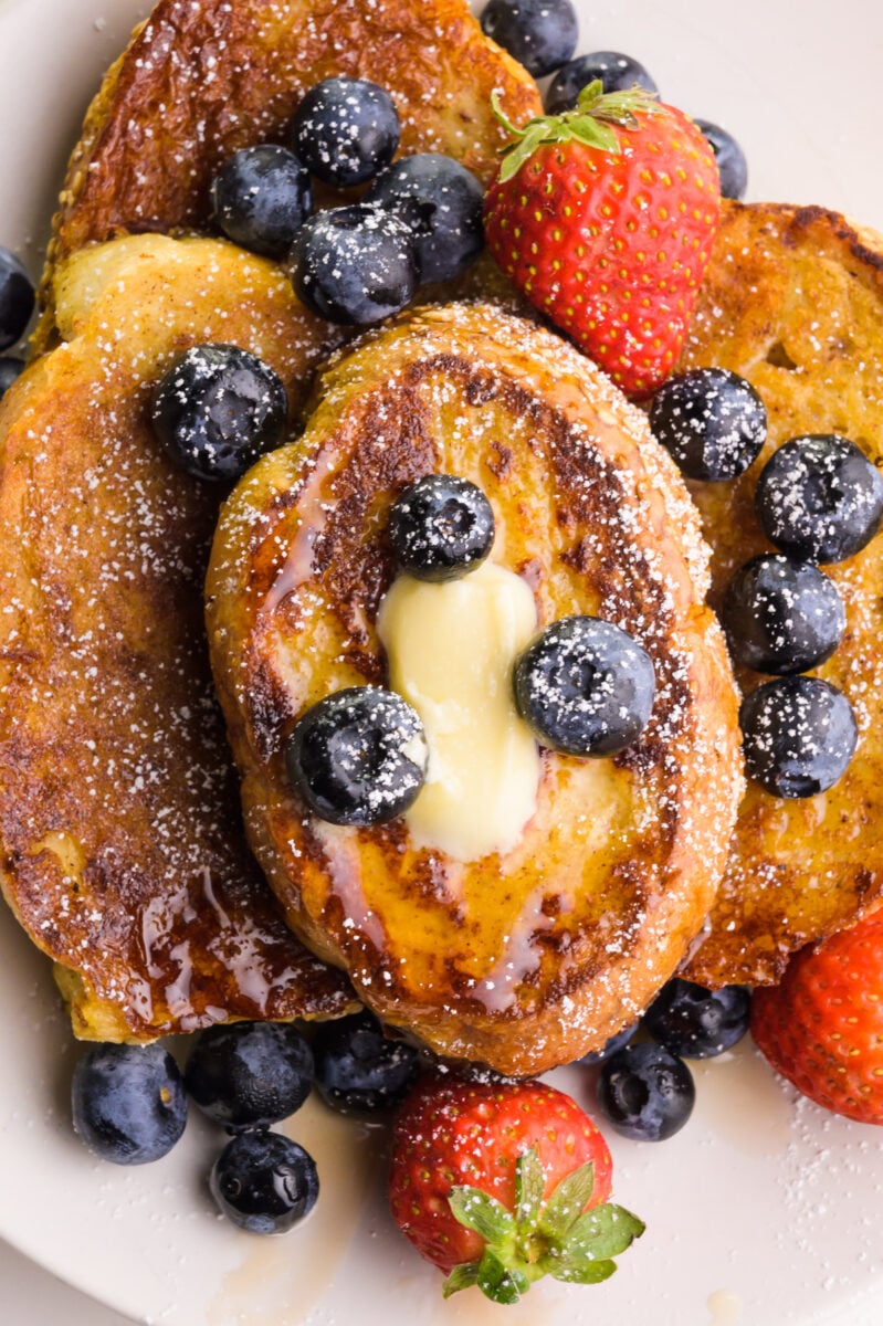 Looking down on slices of French toast on a plate. There are berries and melted butter on top.