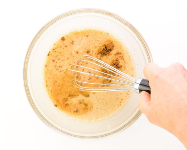 A hand whisks a liquid mixture in a bowl.