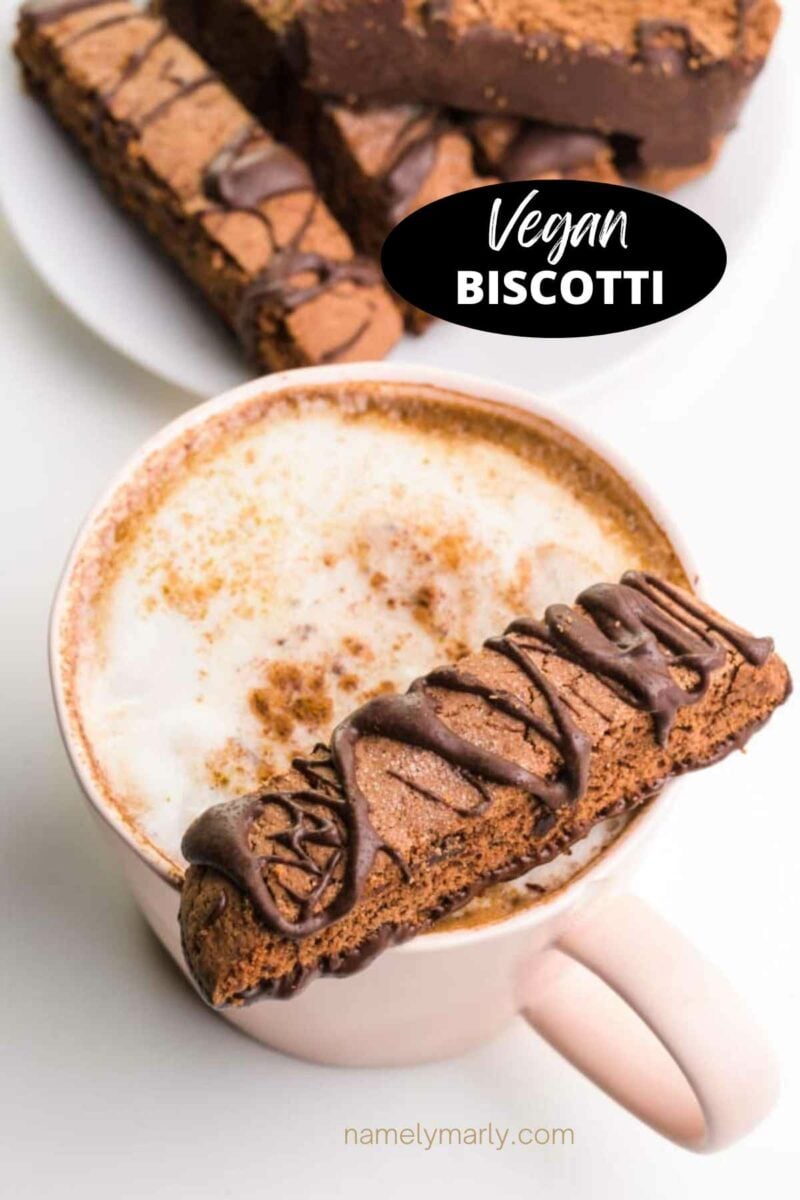 A crisp chocolate cookie sits on a cup of hot tea. There are more cookies in the background. The text reads, Vegan Biscotti.