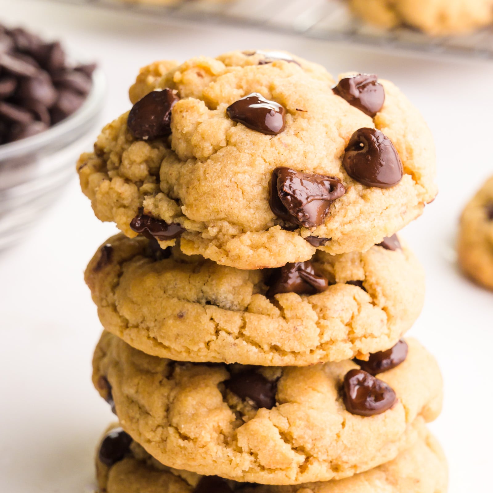 A stack of chocolate chip cookies beside a bowl of chocolate chips.