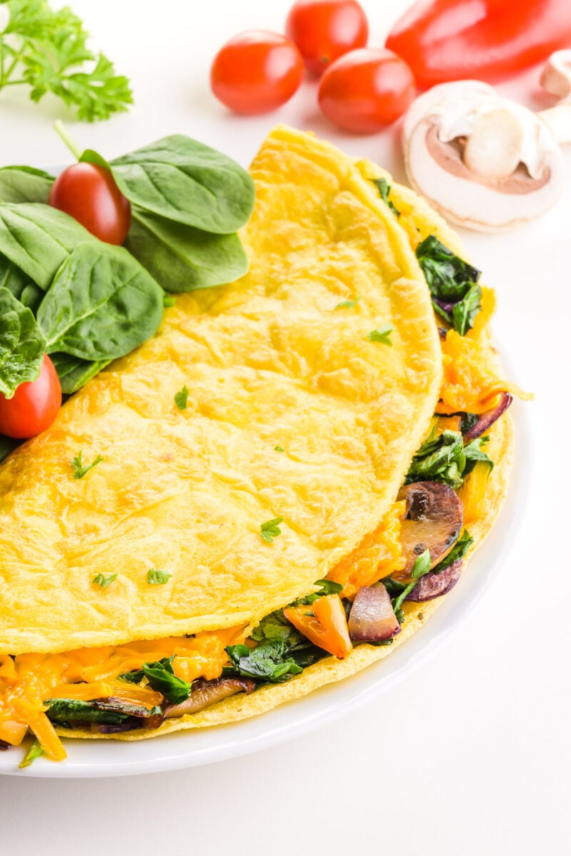 Looking down on an omelette on a plate with greens. There are cherry tomatoes in the background.