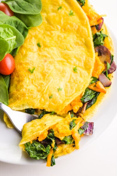 Looking down on an omelette with a bite taken out sitting on a plate.with greens and cherry tomatoes.