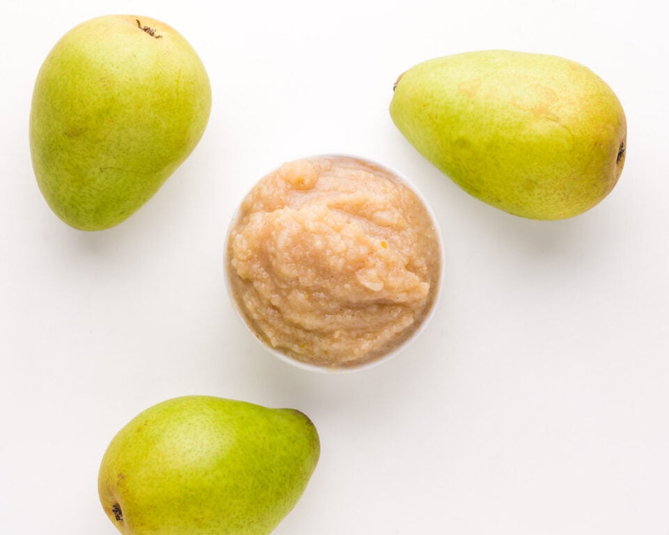 Looking down on a bowl of pear sauce with pears sitting beside it.