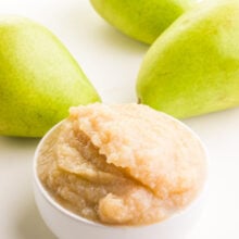 A bowl of pear sauce sits in front of fresh pears in the background.