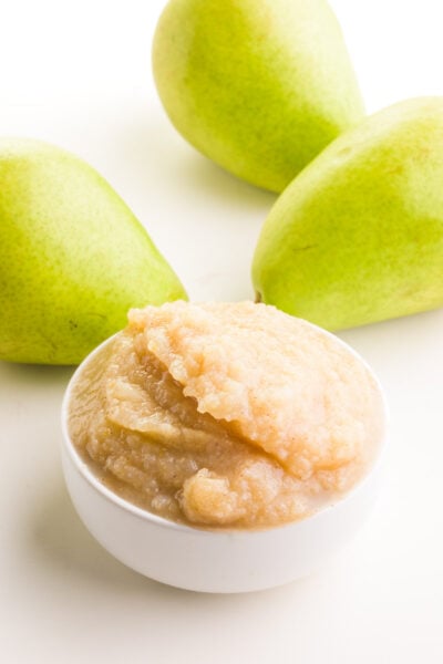 A bowl of pear sauce sits in front of fresh pears in the background.