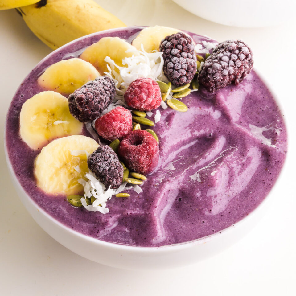 A purple smoothie bowl has frozen fruit on top.
