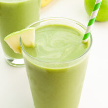 A closeup of a green smoothie in a glass with a straw and an apple wedge.