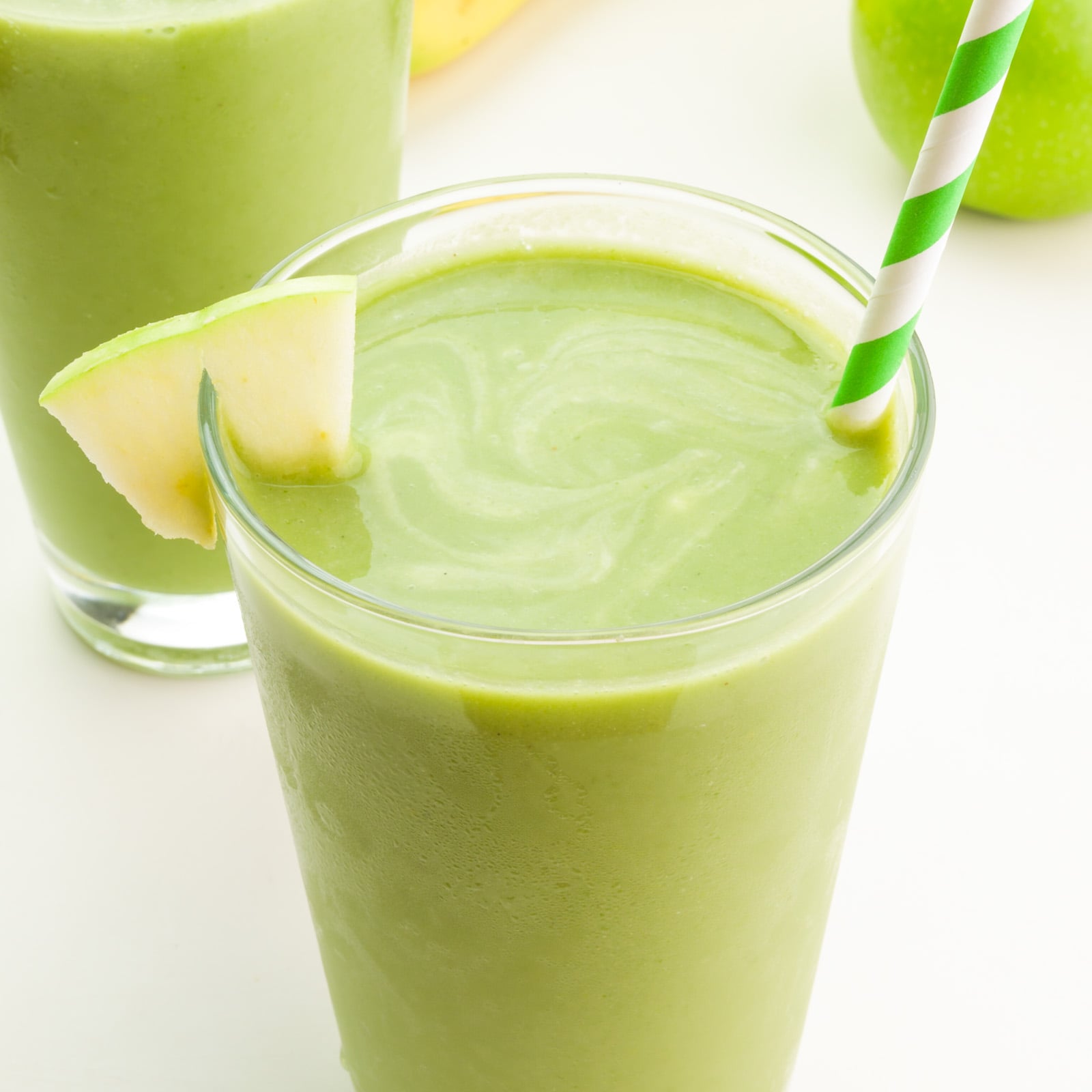 A closeup of a green smoothie in a glass with a straw and an apple wedge.
