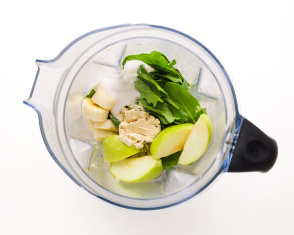 Ingredients like apple slices and spinach are in a blender jar.