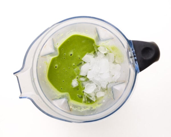 Ice is in a blender jar along with a green smoothie mixture.