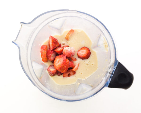 Strawberries are in a blender with other smoothie ingredients.