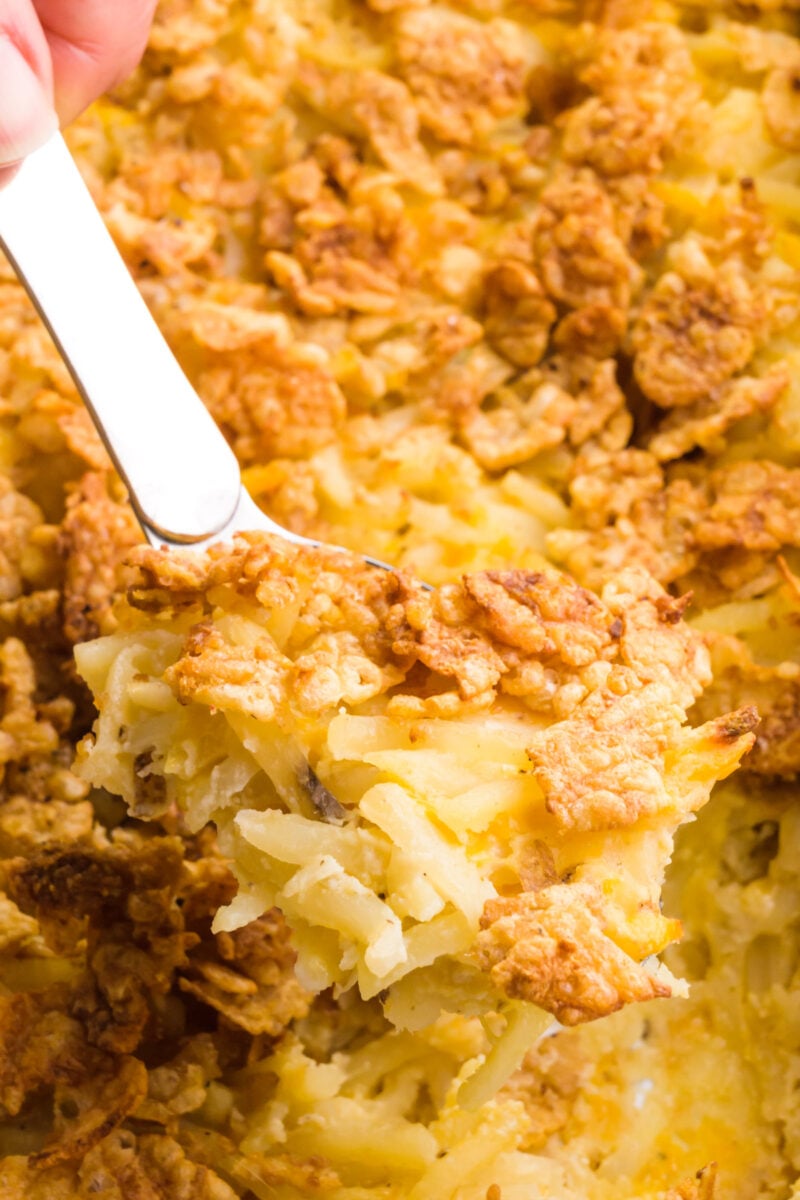 A serving spoon is full of golden crisp potatoes. It hovers over a casserole dish with more of the potatoes.