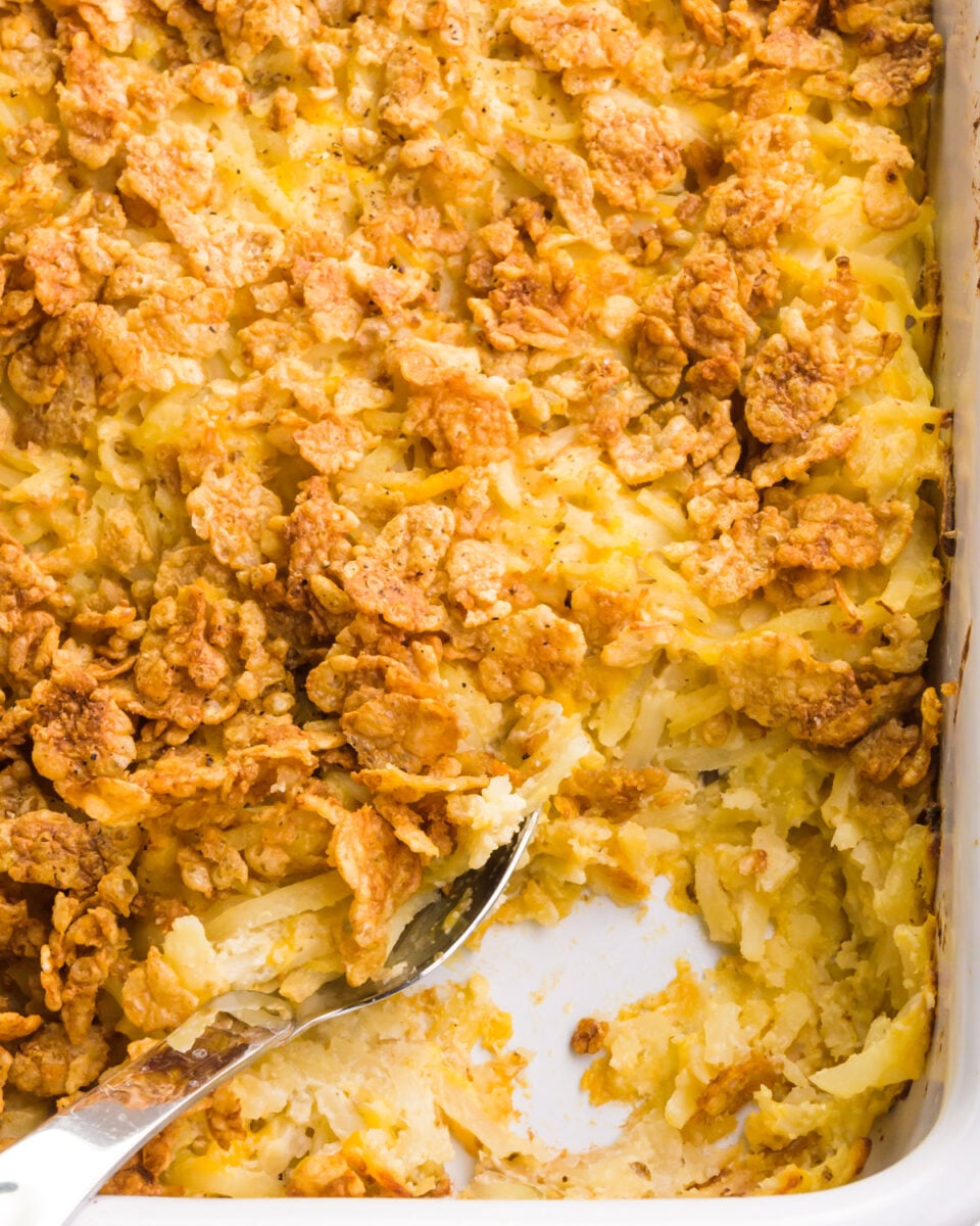Looking down on a casserole dish with vegan cheesy potatoes. A spoon has dished out some of the potatoes, revealing the pan at the bottom.