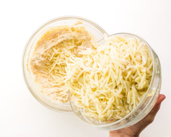 Thawed frozen hash brown potatoes are being poured into a bowl with a creamy mixture.