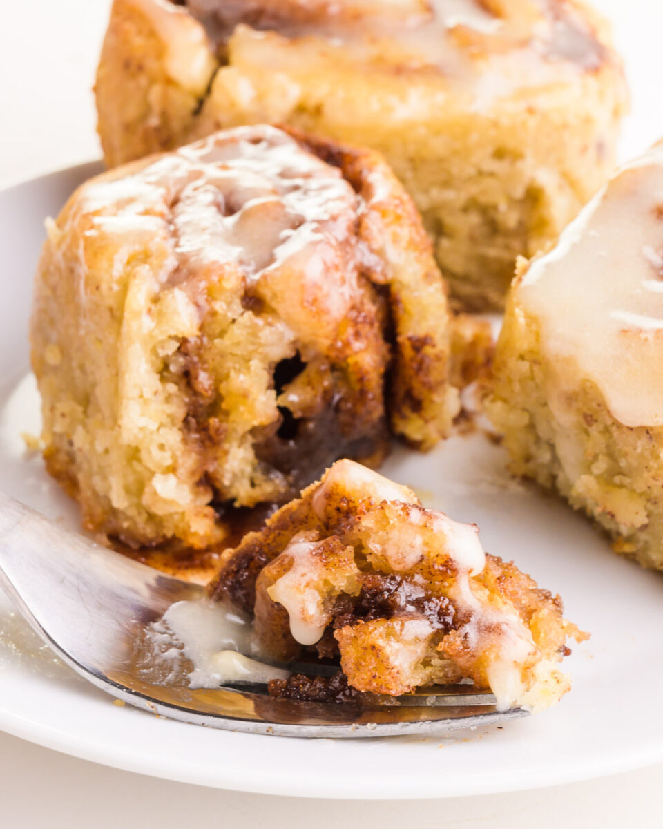 A bite of cinnamon roll sits on a fork in front of rolls on a plate.