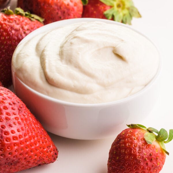 A closeup of mascarpone in a bowl sitting around fresh strawberries.