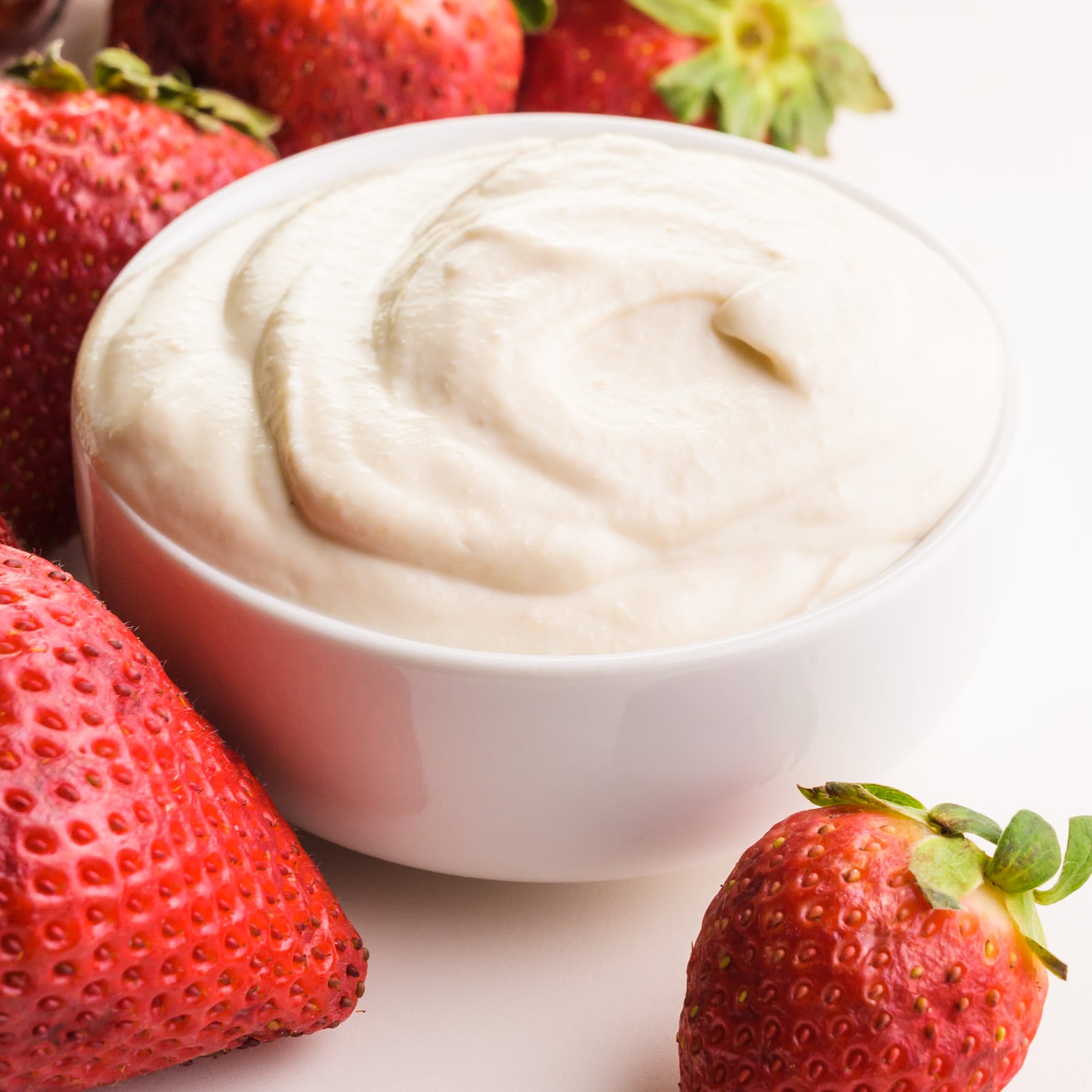 A closeup of mascarpone in a bowl sitting around fresh strawberries.