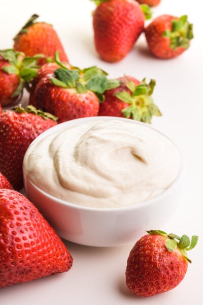 A bowl of vegan mascarpone sits around fresh strawberries.